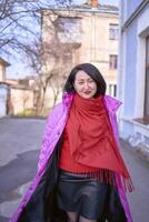 une élégant femme dans une longue brillant rose, magenta manteau et rouge des chaussures des promenades le des rues de le ville photo