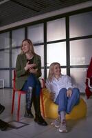 une femme fait du une discours sur organiser, collègues rire à sa blagues séance sur chaises et poufs dans le entrée, Bureau emplacement photo