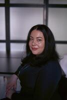 portrait de une moyen Taille femme avec noir cheveux dans une noir robe dans un Bureau photo