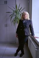 portrait de une blond milieu âge femme dans une affaires costume dans le Bureau photo