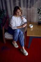 mignonne milieu âge femme chercher sur sa téléphone dans une magnifique café avec verdure et lumière panneaux dans le Contexte photo