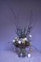 Pâques couronne, nid de saule branches et fleurs décoré avec des œufs et verre tester tubes dans une transparent vase photo