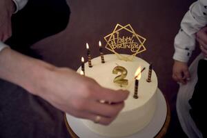 père lumières bougies sur le sien fils seconde anniversaire gâteau photo