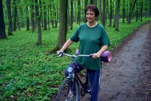 personnes âgées femme en marchant dans printemps forêt avec vélo et yoga tapis photo
