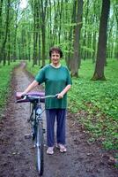 personnes âgées femme en marchant dans printemps forêt avec vélo et yoga tapis photo