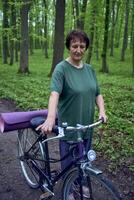 personnes âgées femme en marchant dans printemps forêt avec vélo et yoga tapis photo