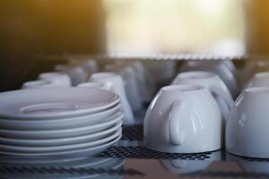 fermer de une blanc café tasses et soucoupes sont mis à l'envers vers le bas sur Haut de le café fabricant avec lumière du soleil Contexte photo