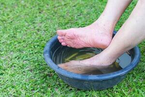 fermer de spa pied avec herbes l'eau pour relaxation traitement. une Sénior femme avec la cheville douleur les usages à base de plantes traitement à se détendre le muscles par trempage chaud l'eau cette est bouilli de herbes photo