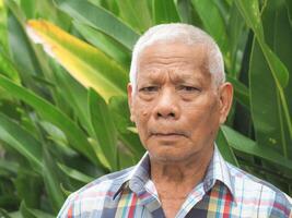 portrait de un personnes âgées asiatique homme souriant et à la recherche à le caméra tandis que permanent dans une jardin. concept de vieilli gens et soins de santé photo