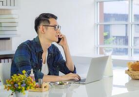 Jeune homme travail sur une portable sur le table et en utilisant une téléphone intelligent tandis que séance sur une chaise dans le bureau. espace pour texte photo