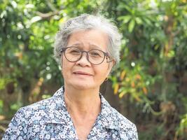 portrait de un personnes âgées asiatique femme souriant et à la recherche à le caméra tandis que permanent dans une jardin. concept de vieilli gens et soins de santé photo