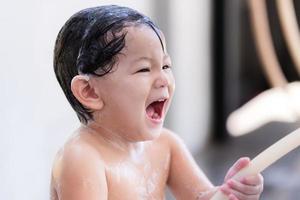 mignon garçon d'âge préscolaire asiatique rient. bébé s'amusant à se baigner et se laver les cheveux. petit enfant doux souriant gai. ses mains tenant un bracelet en caoutchouc pour libérer de l'eau propre. le fils a 2 ans.
