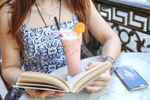 femme en train de lire livre et profiter boisson à table photo