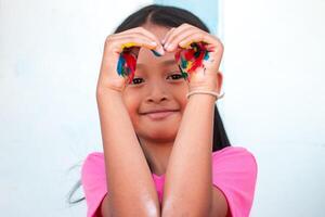 mignonne peu fille avec coloré peint mains sur mur Contexte photo