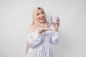 content Jeune asiatique musulman femme dans une voile hijab montrer du doigt à une verre de clair l'eau elle tient. Ramadan publicité concept photo