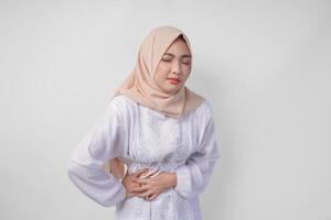 Jeune asiatique musulman femme dans blanc robe et crème voile hijab en portant sa estomac sentiment faim pendant jeûne. Ramadan concept photo