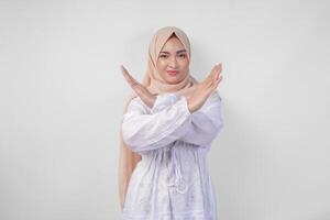 mécontent asiatique femme dans blanc robe et hijab faire des gestes une refus ou rejet signe, en disant Non, demander à Arrêtez en utilisant mains, permanent plus de isolé blanc Contexte photo