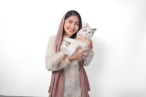 attrayant Jeune asiatique musulman femme dans voile hijab souriant tandis que posant et étreindre une blanc ragdoll chat animal de compagnie photo