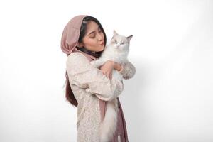 attrayant Jeune asiatique musulman femme dans voile hijab souriant tandis que posant et étreindre une blanc ragdoll chat animal de compagnie photo