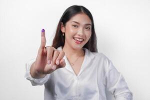 Jeune asiatique femme fièrement montrant peu doigt plongé dans violet encre après vote pour Président et parlement élection, exprimer excitation et bonheur photo