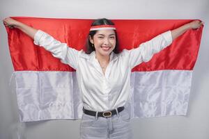 souriant asiatique femme portant drapeau Bandeau et décontractée tenue tandis que en portant Indonésie drapeau à le dos. indépendance journée publicité concept photo