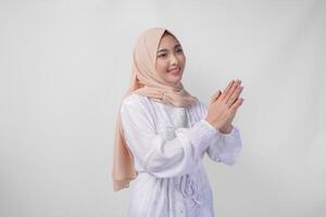 magnifique asiatique musulman femme portant blanc robe et hijab souriant tandis que Faire formel Bienvenue ou salutation geste, permanent plus de isolé blanc Contexte photo