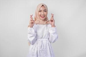 magnifique asiatique femme portant hijab et blanc robe avec les doigts posant une souhait moi la chance geste, permanent plus de isolé blanc Contexte. Ramadan et eid mubarak concept photo