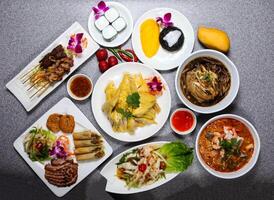 assorti thaïlandais nourriture avec grillé porc cou, poisson gâteau, printemps rouleau, poulet pieds, du boeuf et poulet saté, sagou gâteau, gluant riz avec mangue servi isolé sur Contexte Haut vue de Hong kong nourriture photo