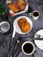 pêche danois Pâtisserie bouffée servi dans assiette avec tasse de noir café isolé sur serviette de table avec fourchette et couteau Haut vue de français petit déjeuner cuit nourriture article sur gris Contexte photo