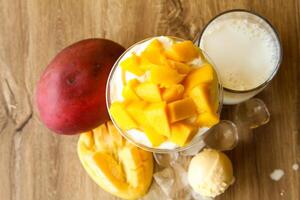 mangue Milk-shake avec la glace crème scoop et la glace cube servi dans jetable verre avec la glace cube isolé sur table Haut vue de en bonne santé Matin Lait secouer boisson photo