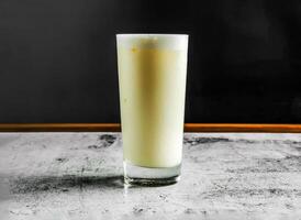 sucré lassi avec yaourt, sucre, l'eau et la glace servi dans verre côté vue sur gris Contexte boisson photo