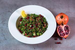 quinoa salade avec Grenade des graines et citron vert tranche servi dans plat isolé sur gris Contexte Haut vue de Bahreïn nourriture photo