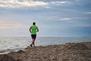 retour vue de homme le jogging le long de mer plage à Matin photo