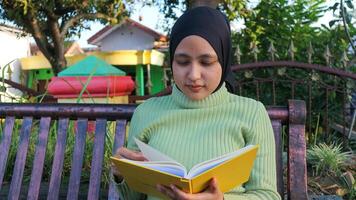 détendu musulman femme profiter fin de semaine à parc, séance sur banc et en train de lire livre, vide espace photo