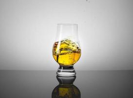 verre de dégustation avec un verre de scotch whisky et un glaçon tombant dedans.