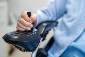 asiatique Sénior femme patient sur électrique fauteuil roulant avec éloigné contrôle à hôpital. photo