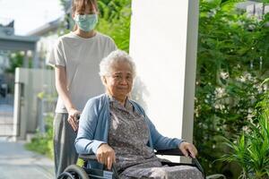 soignant Aidez-moi et se soucier asiatique Sénior femme patient séance sur fauteuil roulant à rampe dans allaitement hôpital, en bonne santé fort médical concept. photo