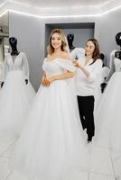 le future mariée choisit une robe pour le mariage. une couturière assistant est raccord une robe pour le la mariée photo