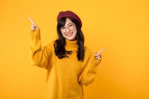 Jeune asiatique femme dans sa 30s, portant une Jaune chemise et rouge béret. content visage et montrer du doigt doigt à gratuit copie espace contre vibrant Jaune toile de fond. ouvrir des économies et magasin maintenant photo