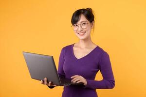 une portrait de une Jeune et sur de soi femme d'affaires, portant une violet chemise et lunettes, en portant une portable contre une Jaune arrière-plan, signifiant sa compétence et connaissance dans le numérique monde. photo