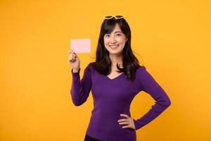magnifique jolie souriant asiatique femme 30s portant violet chemise montrant Vide cadeau carte isolé sur Jaune Contexte. photo