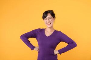 incorporant confiance et de bonne humeur 30s asiatique femme portant violet chemise. avec main sur hanche contre Jaune arrière-plan, rayonne positivité et confiance en soi. sur de soi concept. photo