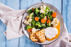 proche en haut de mélanger de bouilli légumes, poché Oeuf et gaufre pain grillé sur une assiette sur le table Haut vue photo