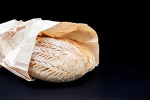 fraîchement cuit Vermont seigle pain avec croustillant croûte et poreux texture dans farine et bemag sac sur noir Contexte. fraîchement cuit fait maison pain dans une kraft papier sac. photo dans haute qualité.
