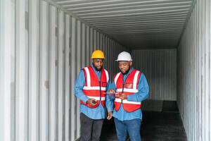 portrait de deux africain ingénieur ou contremaître porte ppe vérification récipient espace de rangement avec cargaison récipient Contexte à le coucher du soleil. logistique global importer ou exportation livraison industriel concept. photo