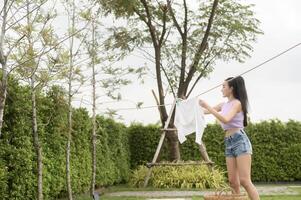 Jeune asiatique femme pendaison blanchisserie sur la lessive ligne pour séchage contre bleu ciel Extérieur photo