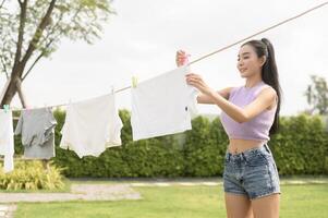 Jeune asiatique femme pendaison blanchisserie sur la lessive ligne pour séchage contre bleu ciel Extérieur photo