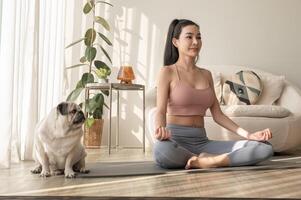 asiatique femme dans tenue de sport exercice et Faire yoga avec mignonne chien dans vivant pièce à maison, en bonne santé mode de vie, mental santé concept. photo