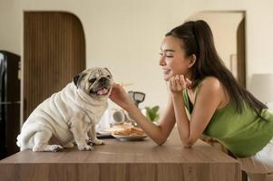 asiatique femme en train de préparer café et pain grillé pain pour petit déjeuner prendre plaisir avec chien à le cuisine table dans le Matin photo