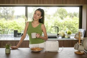 asiatique femme en train de préparer café et pain grillé pain pour petit déjeuner à le cuisine table dans le Matin photo